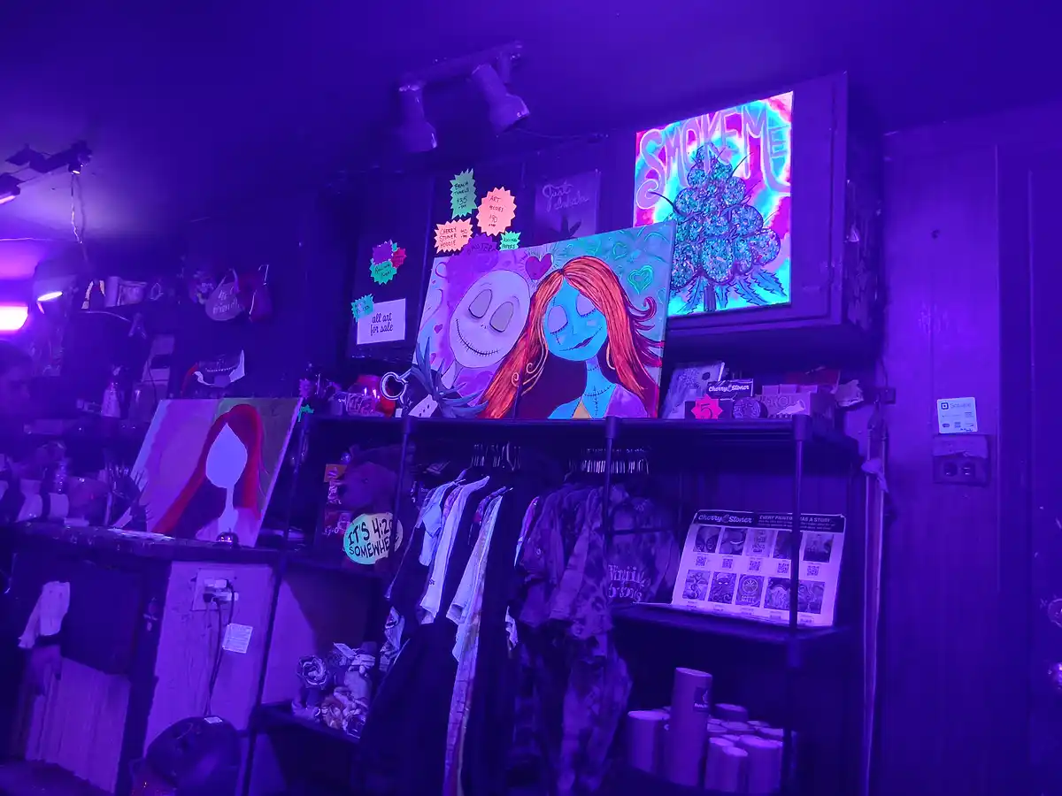 A dimly lit shop bathed in purple light displays artwork, including a prominent painting of Jack and Sally from The…