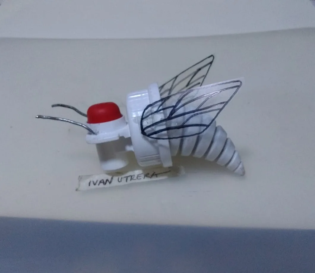 A handmade insect model crafted from a white plastic bottle cap, a red button, and wire antennae, with hand-drawn wings…