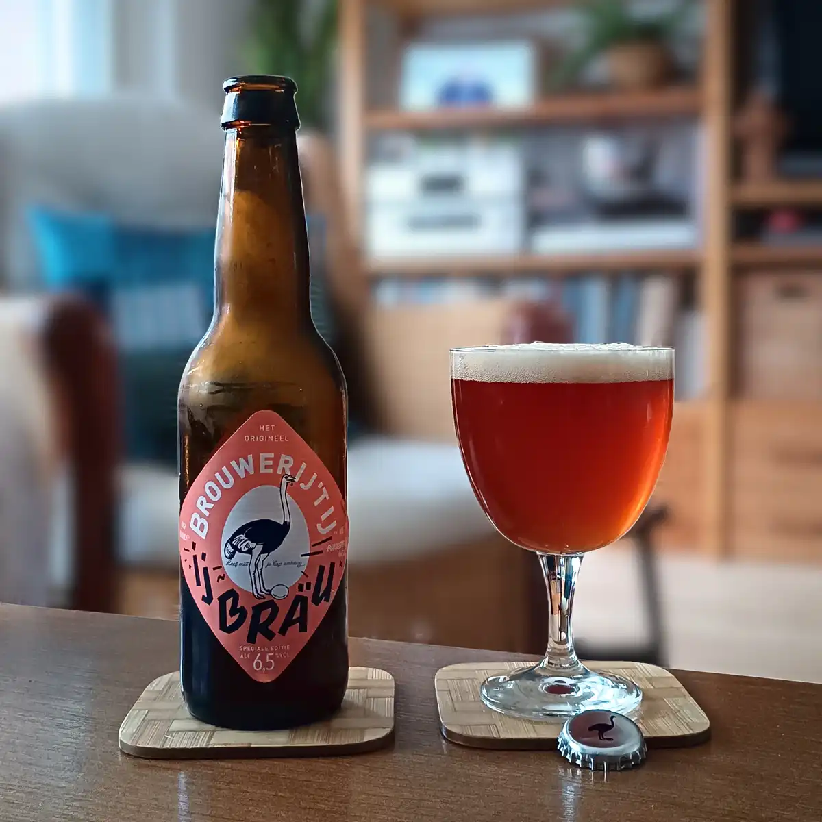 A brown beer bottle with a pink diamond-shaped label featuring an ostrich and the text 'Brouwerij'tuibräu' sits next to a…