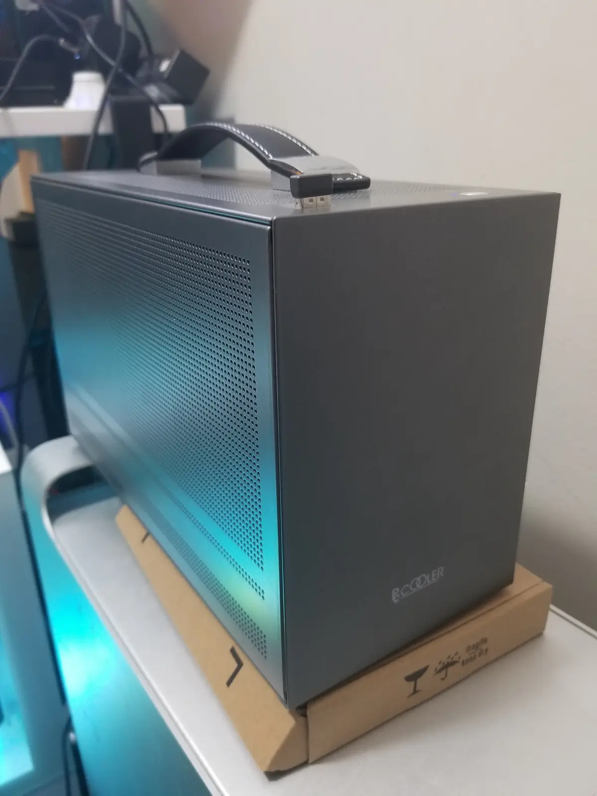 A black computer case with a leather handle and glowing blue interior sits atop a cardboard box labeled 'fragile keep dry'…