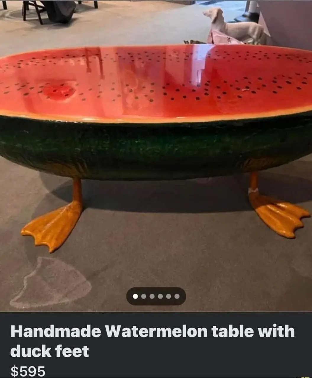 A large, glossy table shaped like a sliced watermelon with a red interior and black seeds, supported by two orange duck feet…