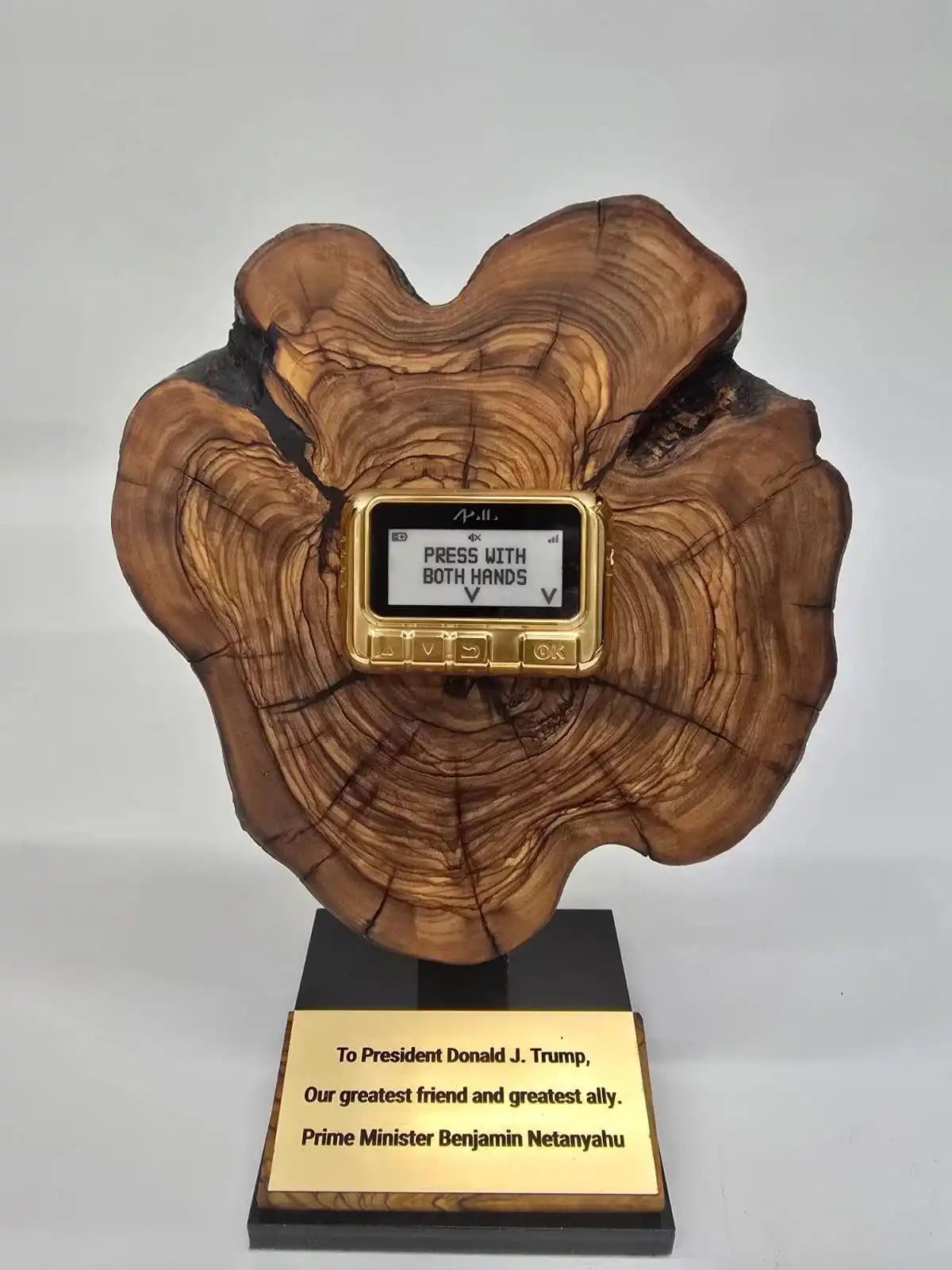 A golden, old-style phone embedded in a wooden tree stump base, displaying the text 'PRESS WITH BOTH HANDS' on its screen…