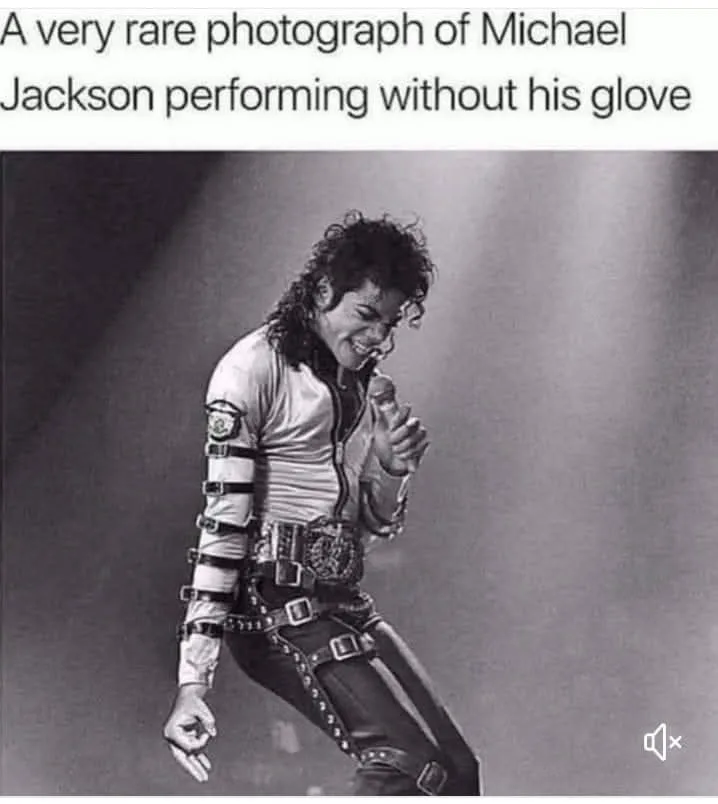A black-and-white photograph of Michael Jackson mid-performance, smiling and holding a microphone. He wears his signature…