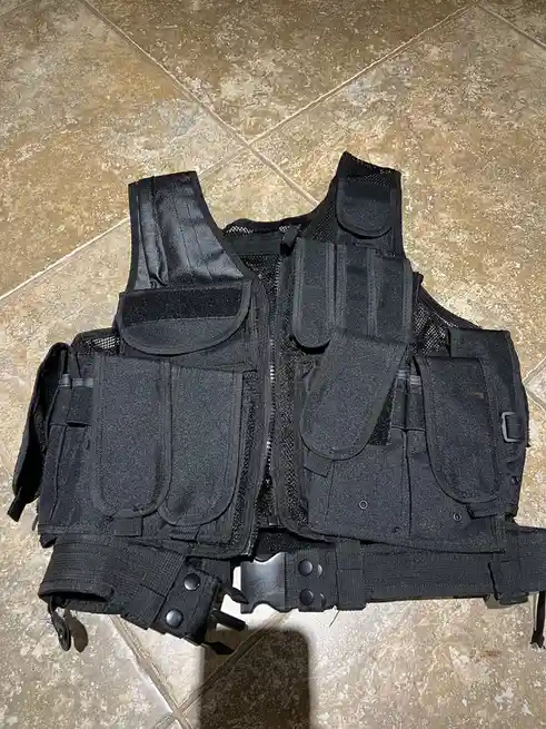A black tactical vest with multiple pockets and straps lies flat on a tiled floor. Overlaid text reads 'i bought this…