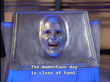 A silver-faced, bald character with wide eyes and an open-mouthed expression is shown inside a framed, metallic-looking box…