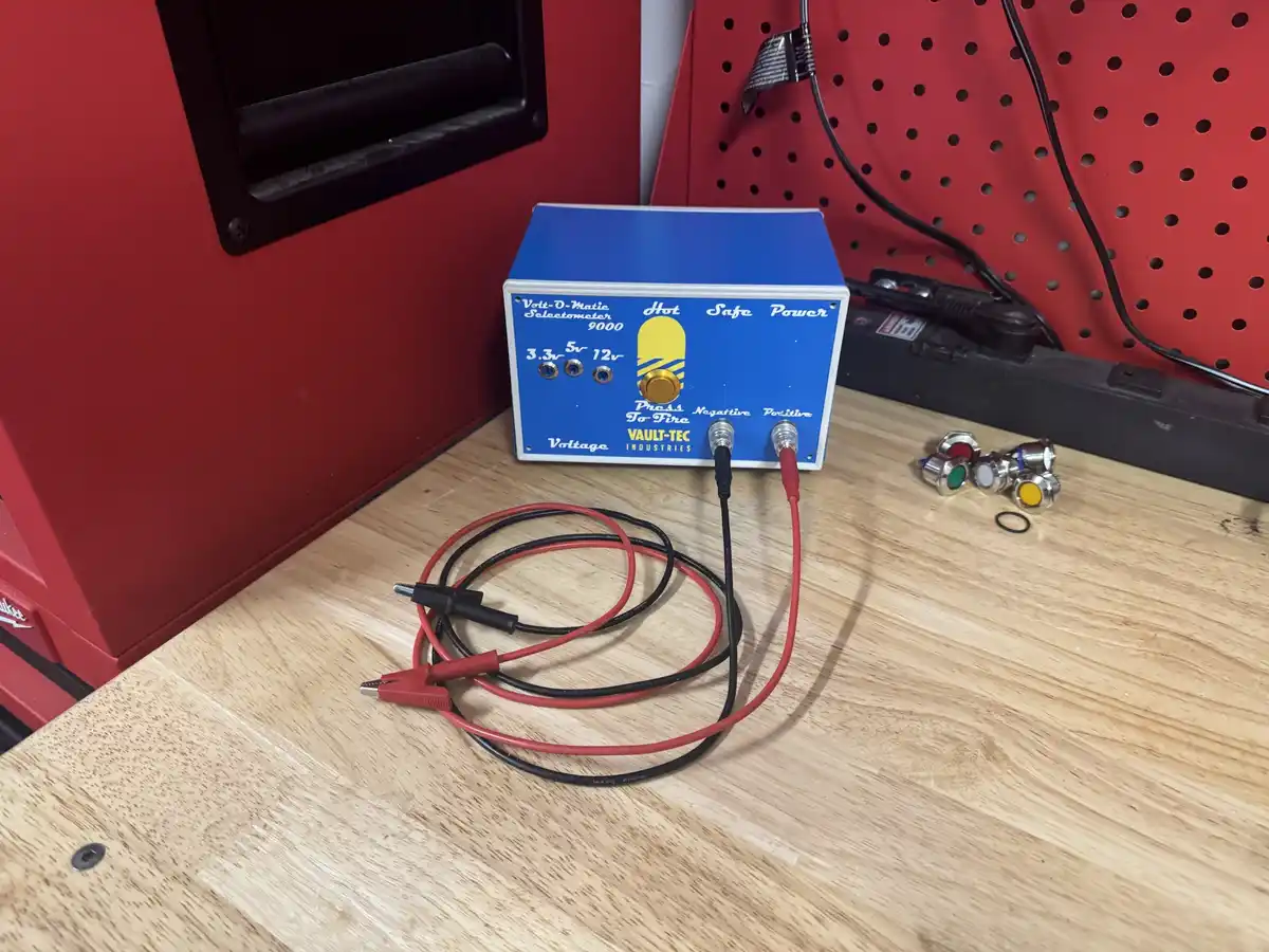 A blue box labeled 'Volt-D-Matic Selectometer 9000' by Vault-Tec Industries sits on a wooden workbench, featuring voltage…