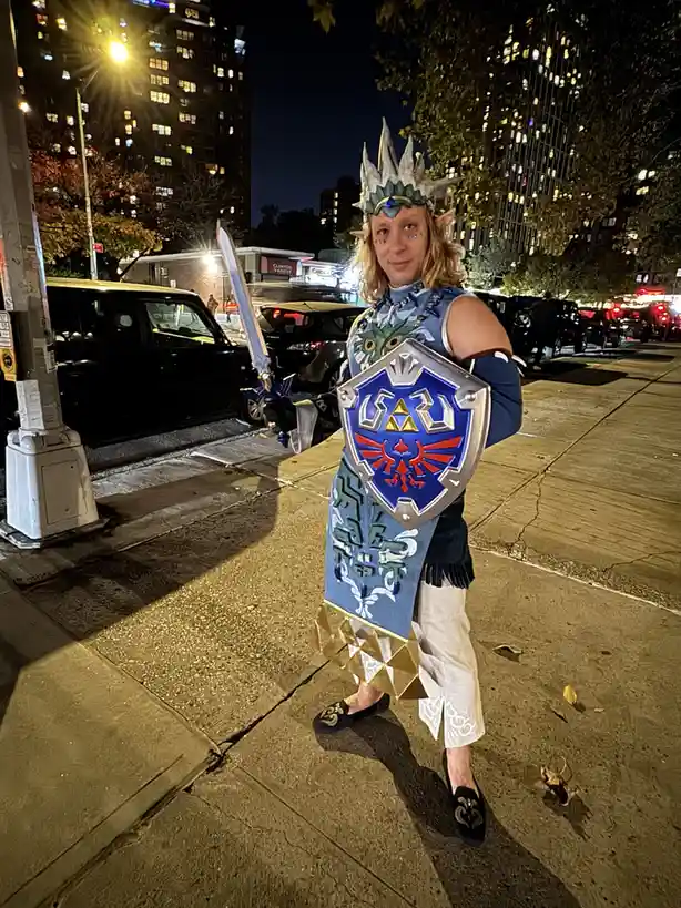 A person dressed as Link from The Legend of Zelda, complete with a blue tunic, pointed ears, a silver crown, and holding a…