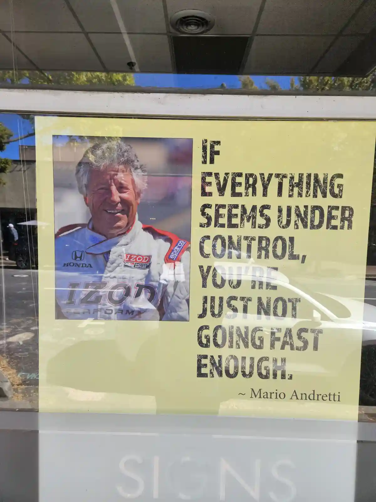 A yellow poster taped to a glass window features a photo of racing driver Mario Andretti in a white racing suit with Honda…