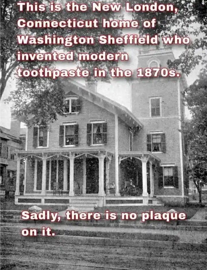 A black-and-white photo shows a large, two-story Victorian-style house with a wraparound porch and multiple windows. Red…