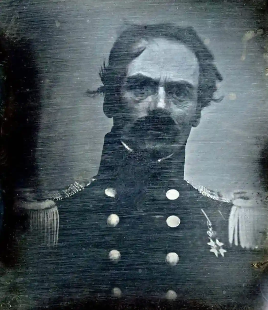 A grainy, vintage black-and-white portrait of a man in a formal military uniform with epaulets and a star-shaped medal…