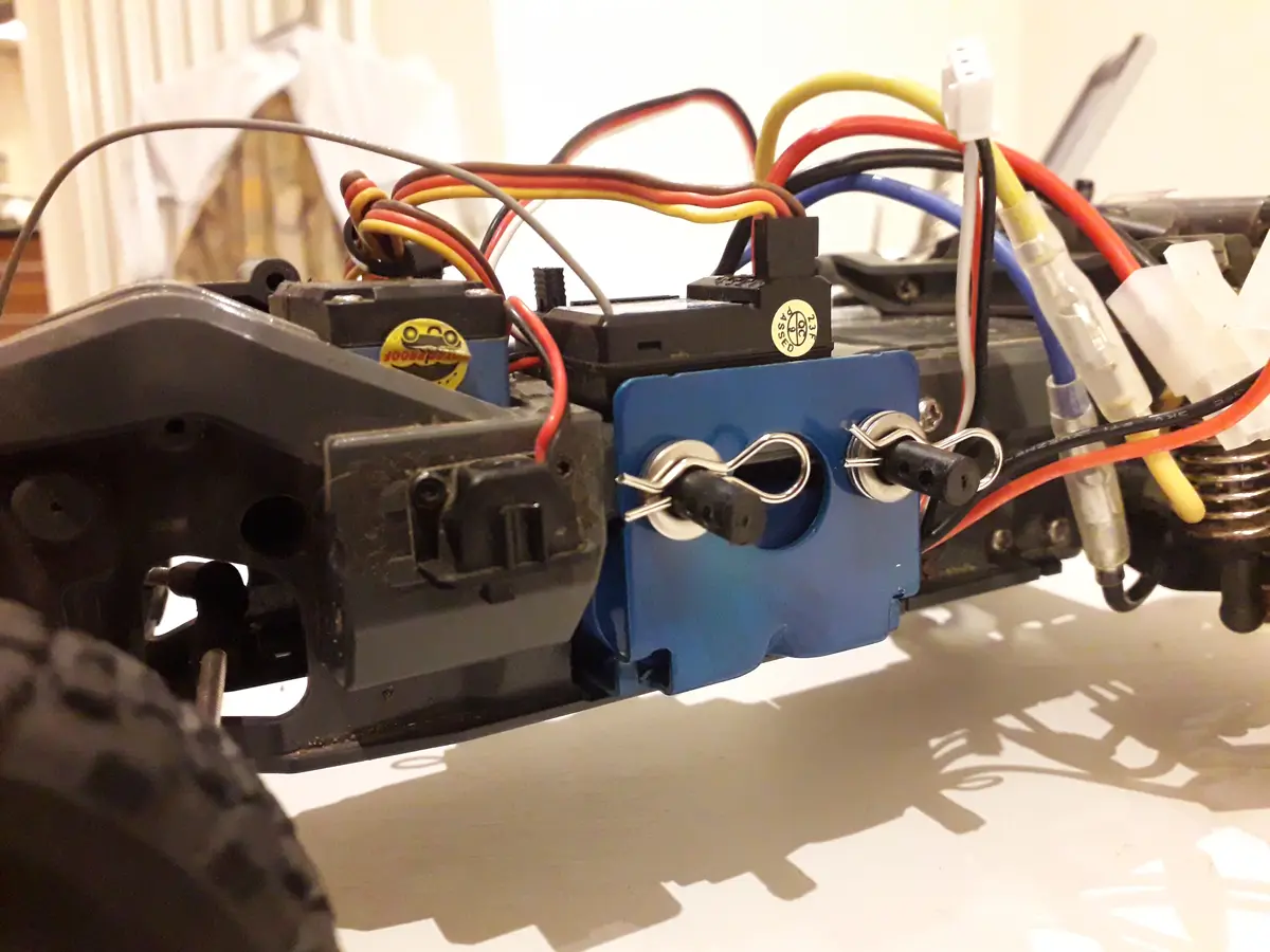 A close-up photo of the internal wiring and components of a remote-controlled car, showing a blue plastic box with two black…