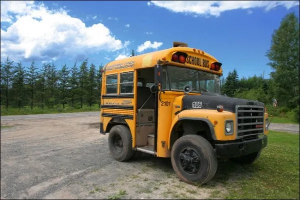 A yellow school bus is parked on a gravel lot with trees and blue sky in the background. The bus has visible numbers '2101'…