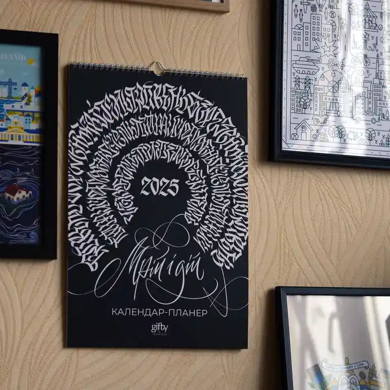 A black spiral-bound planner hangs on a patterned wall, featuring intricate white calligraphy forming a circular design…