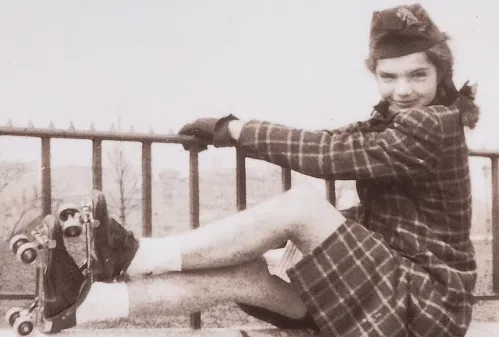 A vintage black-and-white photo shows a young woman in a plaid outfit and hat, sitting on a railing with one leg extended…