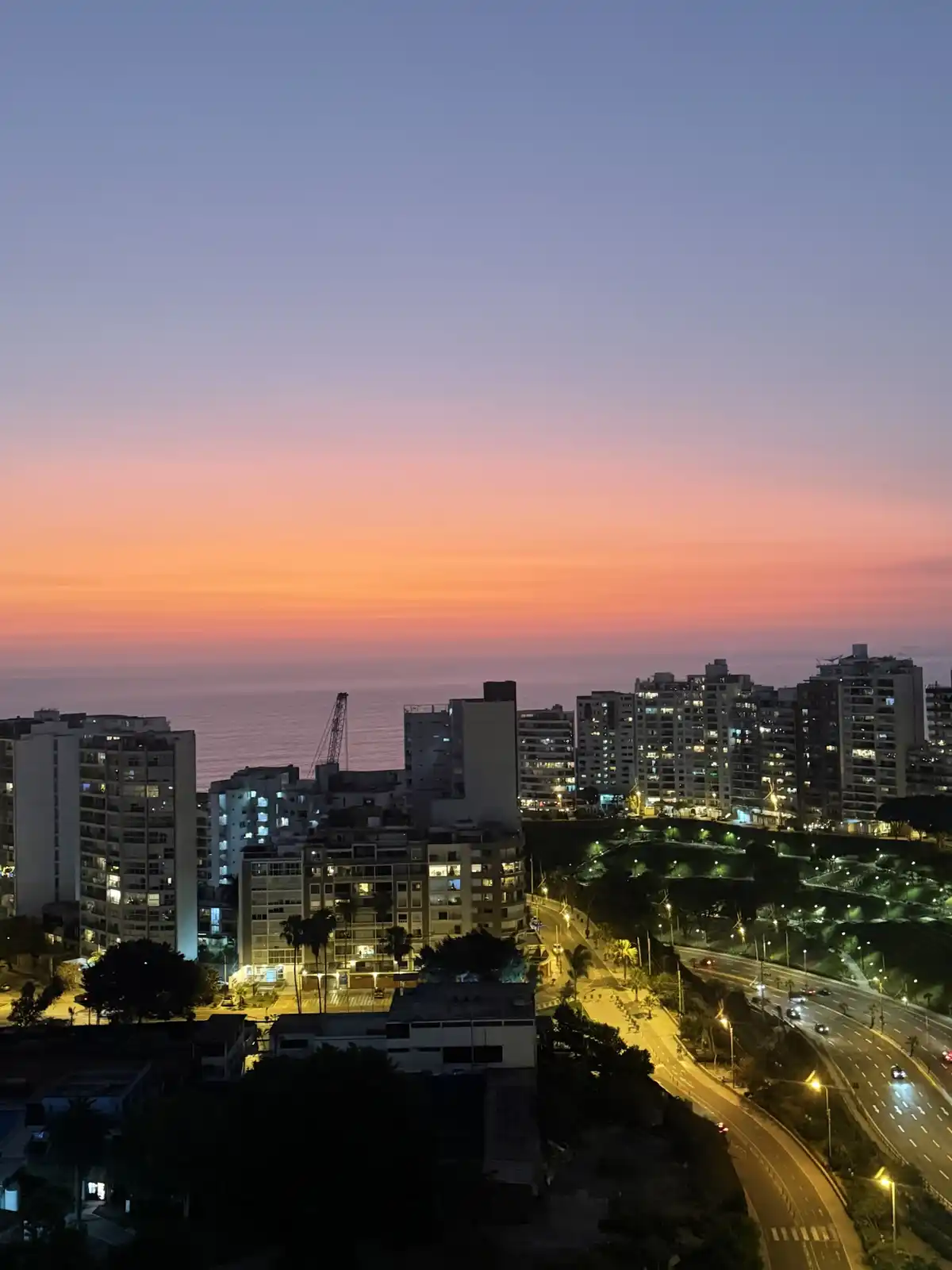 A scenic photo of a city skyline at dusk, with a vibrant gradient sky transitioning from orange to purple above a coastal…