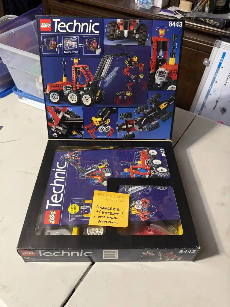 An open LEGO Technic set box (set #8443) displays the completed red and black construction vehicle model inside. A yellow…