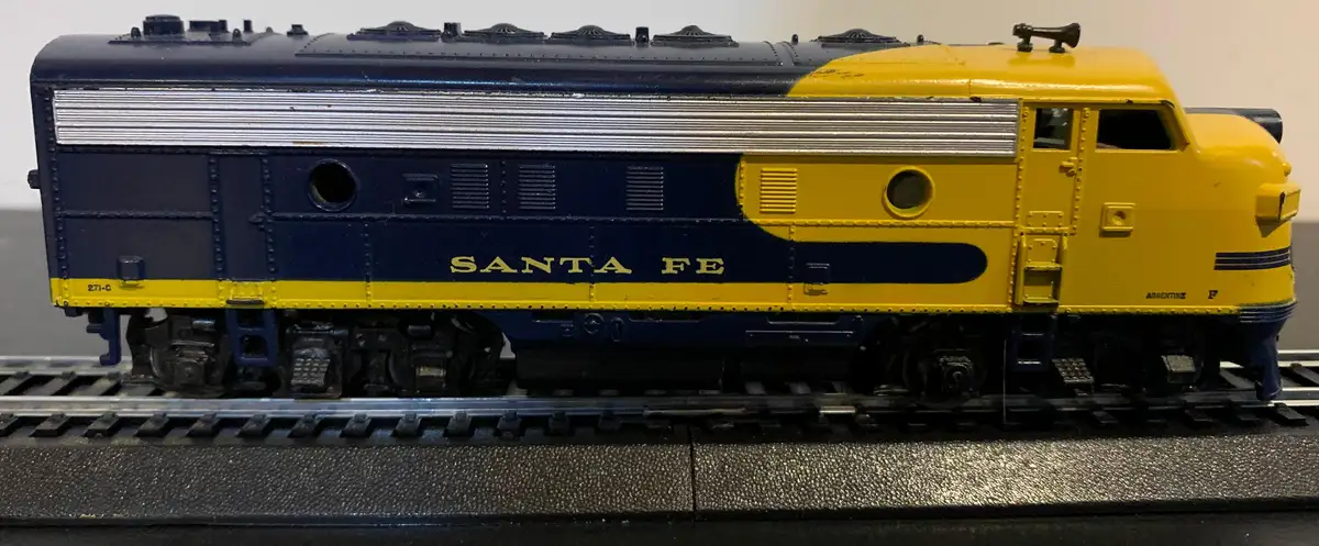 A close-up of a detailed model train locomotive, painted in blue and yellow with 'SANTA FE' written in gold letters on its…