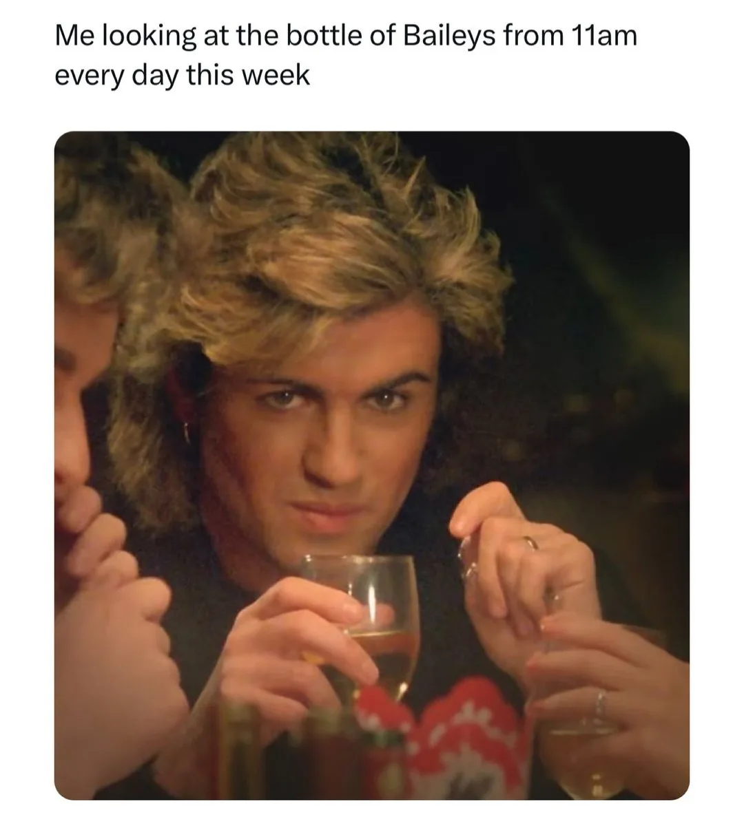 A man with voluminous blonde hair and a serious, intense stare holds a glass of champagne while others around him also hold…