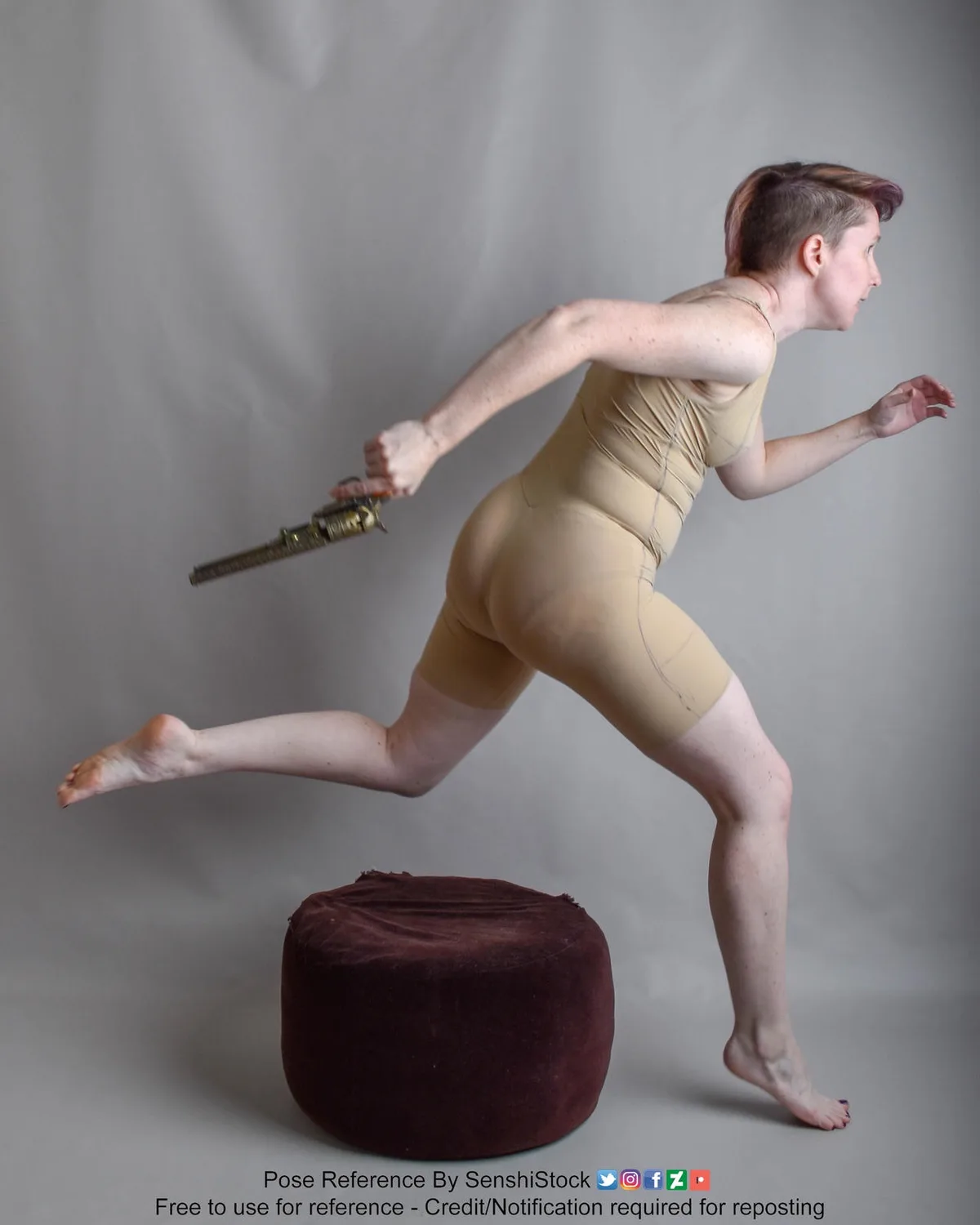A person with short hair in a beige bodysuit is captured mid-stride, appearing to run while holding a revolver, with one…