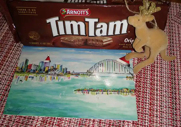 A box of Arnott's Tim Tam biscuits sits atop a watercolor painting of Sydney Harbour with the Harbour Bridge and Opera…