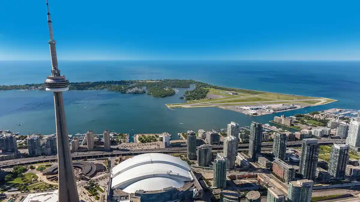 An aerial photo of Toronto, Canada, showing the CN Tower, downtown skyline, and the airport on an island in the water…