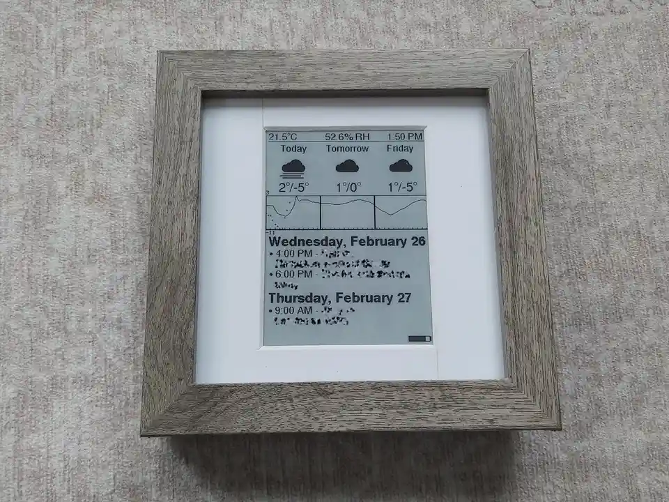A digital weather station display, framed in wood and mounted on a textured wall, shows current conditions of 21.5°C and…