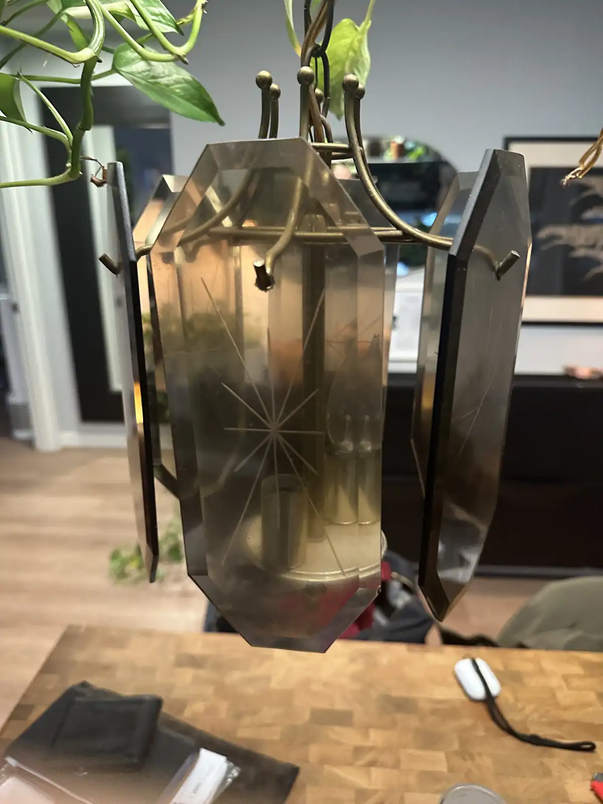 A brass and glass hanging lantern with a starburst etching sits on a wooden table, surrounded by household items like a…