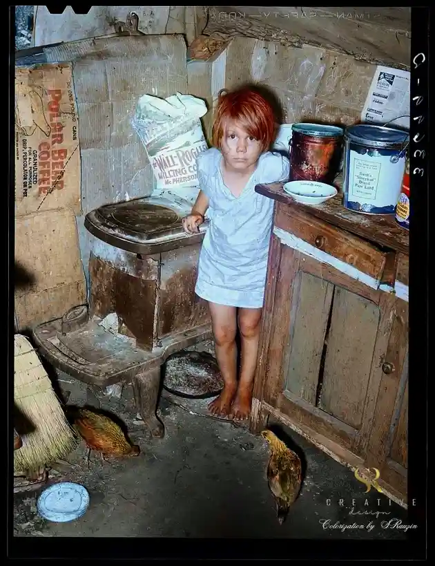 A colorized historical photograph shows a young girl with red hair and dirt-streaked face standing barefoot in a…