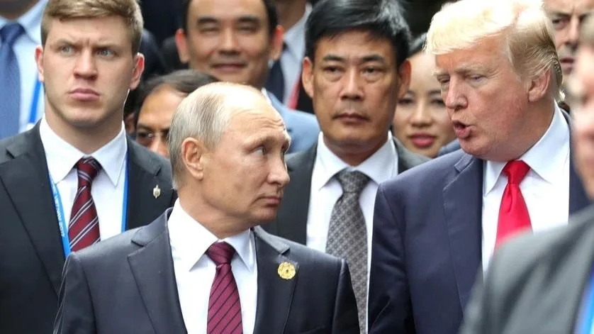 A photo shows Donald Trump speaking while Vladimir Putin looks away with a skeptical expression. Trump is on the right…