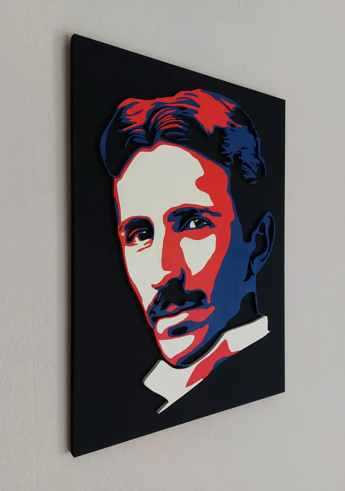 A 3D pop-art style portrait of Nikola Tesla, rendered in red, white, and blue with layered cutouts, mounted on a black…
