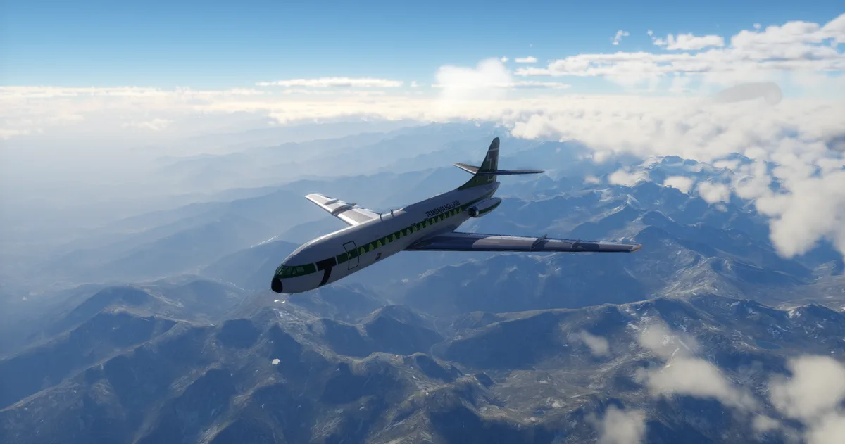 A white and green Transavia Holland airplane flies above a mountain range under a blue sky with scattered clouds. The…