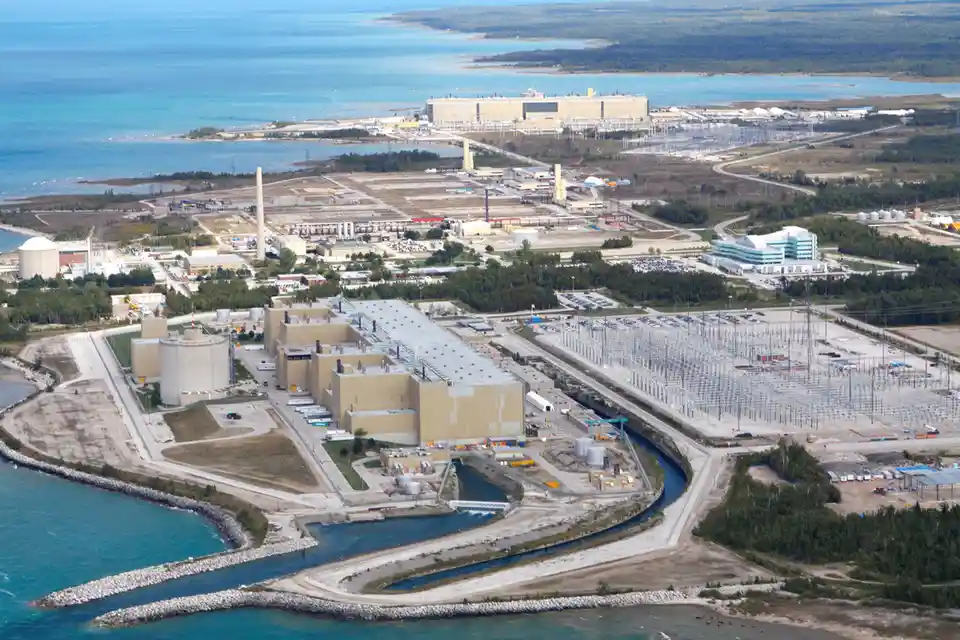 an aerial view of a large nuclear power plant complex situated on a coastal area with a large body of water nearby…