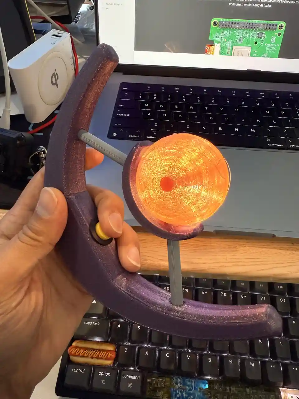 A hand holds a 3d-printed purple hammer with a glowing orange, textured circular head, positioned over a black keyboard. The…