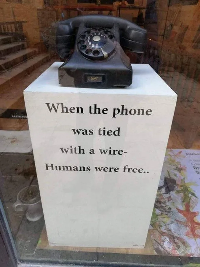 A vintage black rotary telephone sits atop a white pedestal in a store window. The pedestal has black text that reads: 'When…