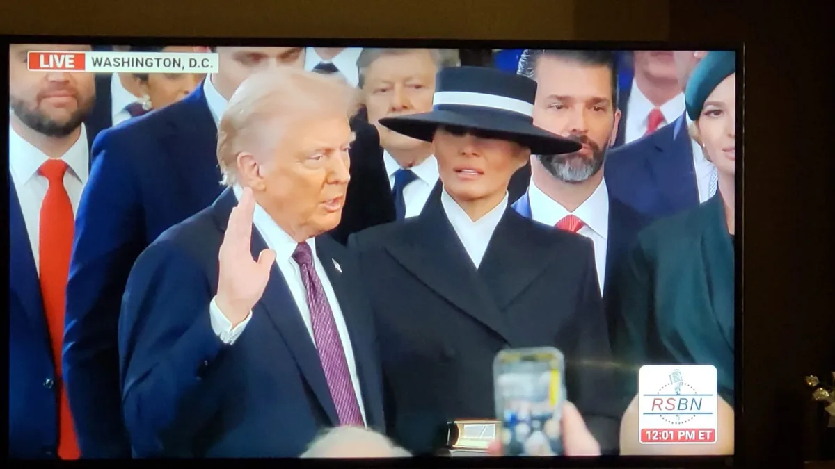 A television broadcast shows Donald Trump raising his right hand as if taking an oath, with Melania Trump standing beside…