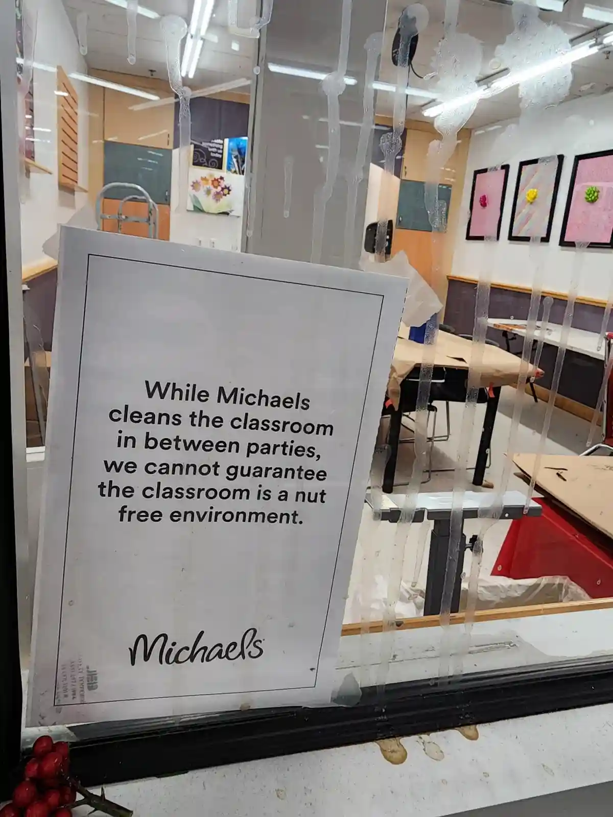 A sign from Michaels, a craft store, is taped to a classroom window covered in cleaning residue. The sign humorously states…
