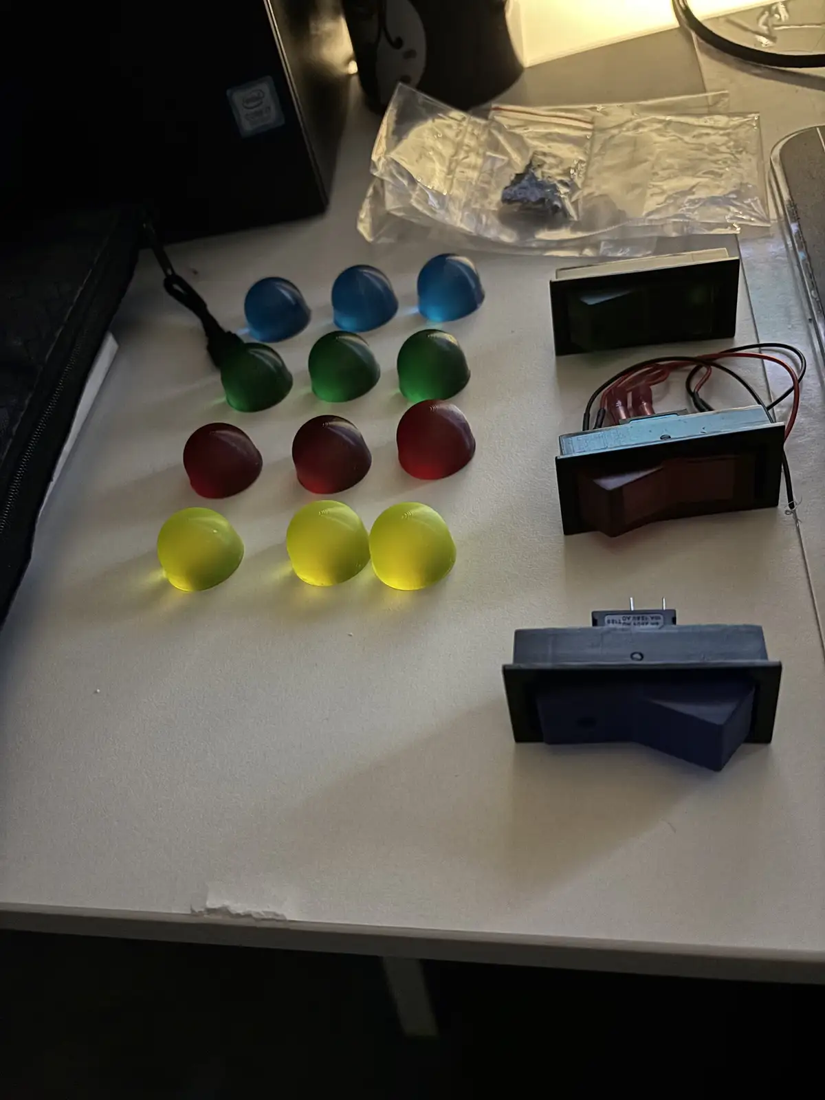 A white desk holds several rows of translucent, dome-shaped jelly-like objects glowing in blue, green, red, and yellow. To…