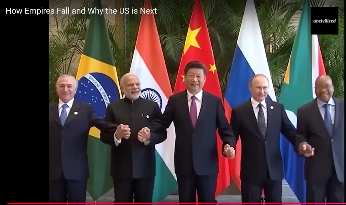 Five world leaders stand side-by-side holding hands in front of their national flags, which include Brazil, India, China…