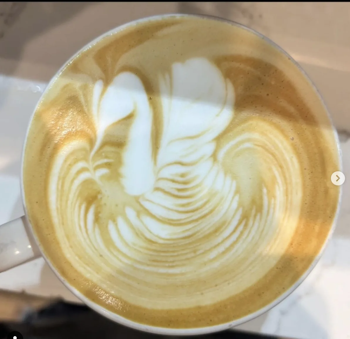 a top-down view of a coffee cup with intricate latte art resembling a flower or leaf, created with white milk foam on top of…