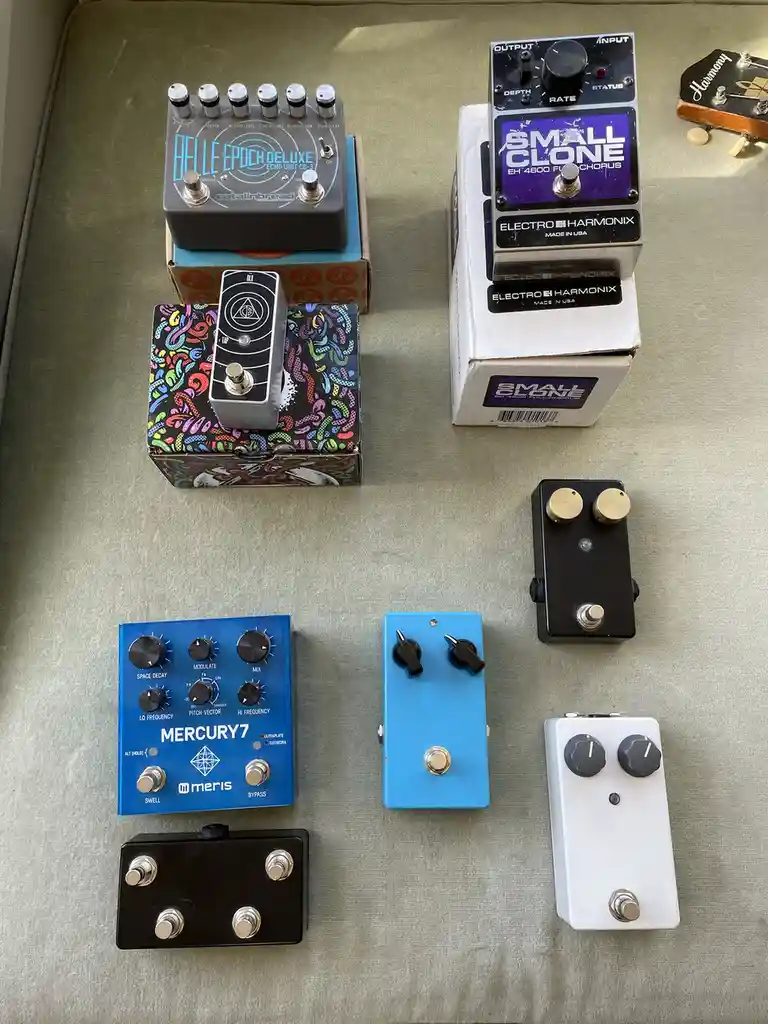 An overhead photo displays eight different guitar effects pedals arranged on a beige fabric surface, including a 'Belle…