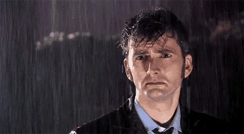 The image shows a man in a dark suit and tie standing in heavy rain, his hair wet and expression somber. The top row…