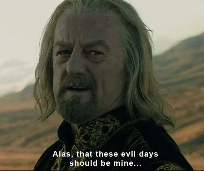A close-up of a man with long grey hair and a beard, wearing ornate dark clothing, looking off-camera with a resigned…