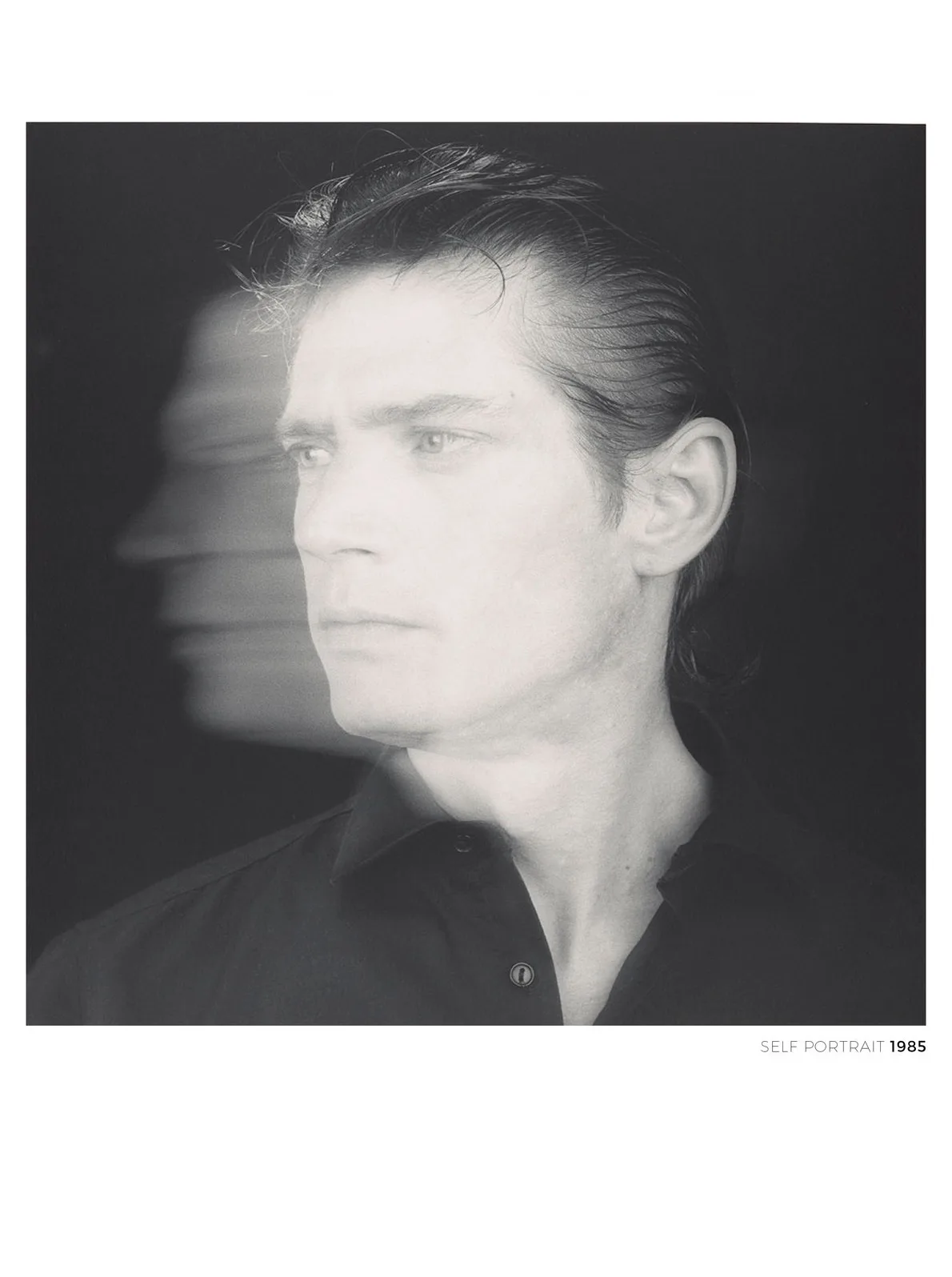 A black and white photograph shows a man in profile, looking off to the side, with a blurred, ghostly image of another face…