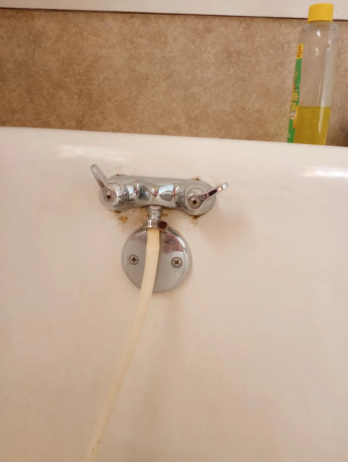 A close-up photo shows a chrome bathtub faucet with visible rust stains around its base and handles, attached to a white…