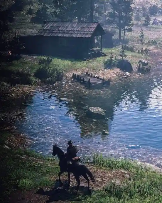 A screenshot from a video game shows a character in a cowboy hat riding a horse near a riverbank with a wooden cabin in the…