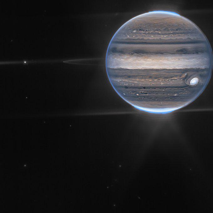 A realistic image of the planet Jupiter, showing its swirling bands and the Great Red Spot, with a bright blue atmospheric…