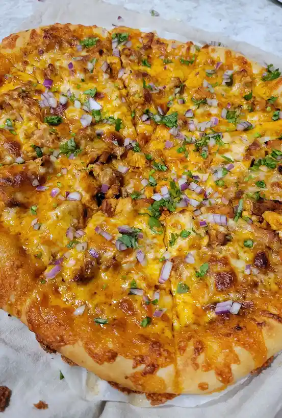 A close-up photo of a freshly baked, sliced pizza with melted orange cheese, chunks of meat, chopped red onions, and green…