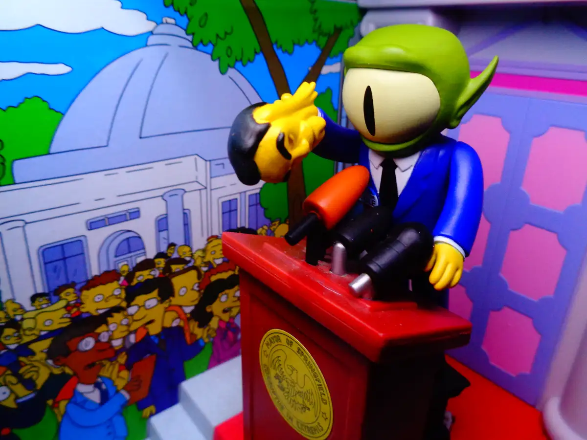 A green-skinned, elf-eared figurine in a blue suit stands at a red podium labeled 'MAYOR OF SPRINGFIELD' with microphones…