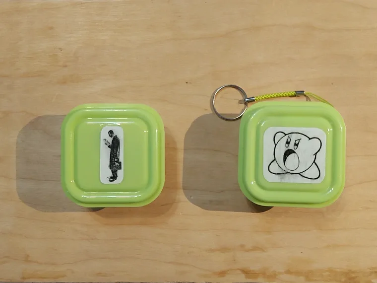 Two lime-green, square-shaped keychains sit side-by-side on a wooden surface. The left keychain features a black-and-white…