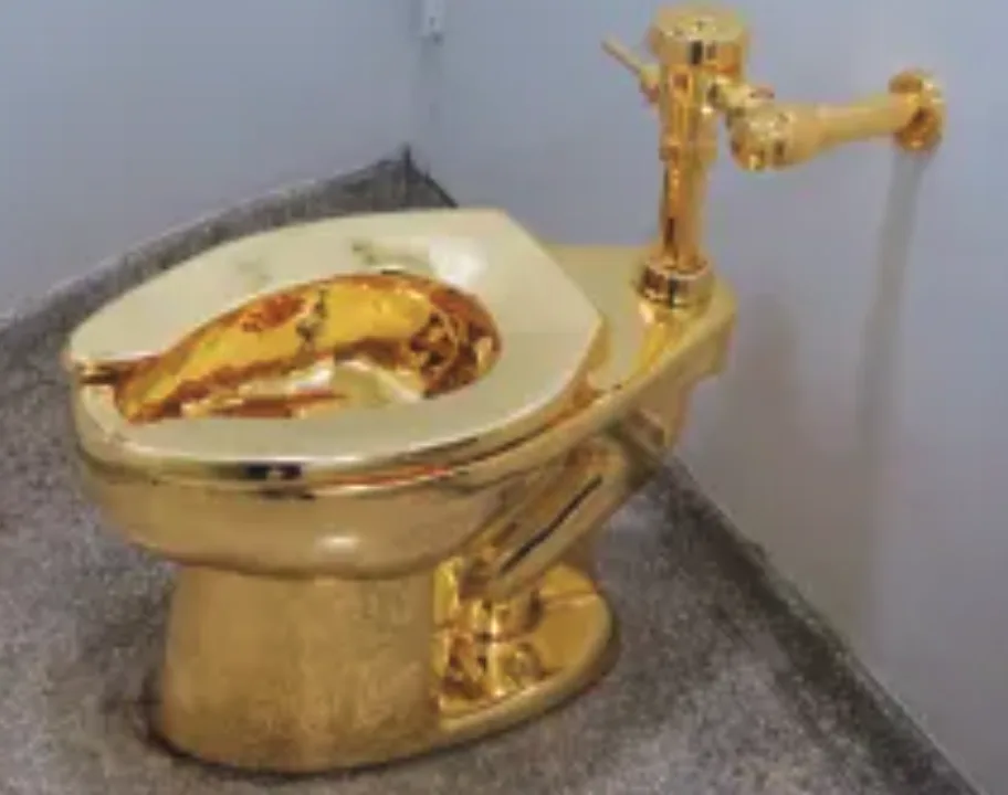 a toilet entirely covered in gold plating sits in a corner, its bowl visibly corroded and tarnished with dark spots…